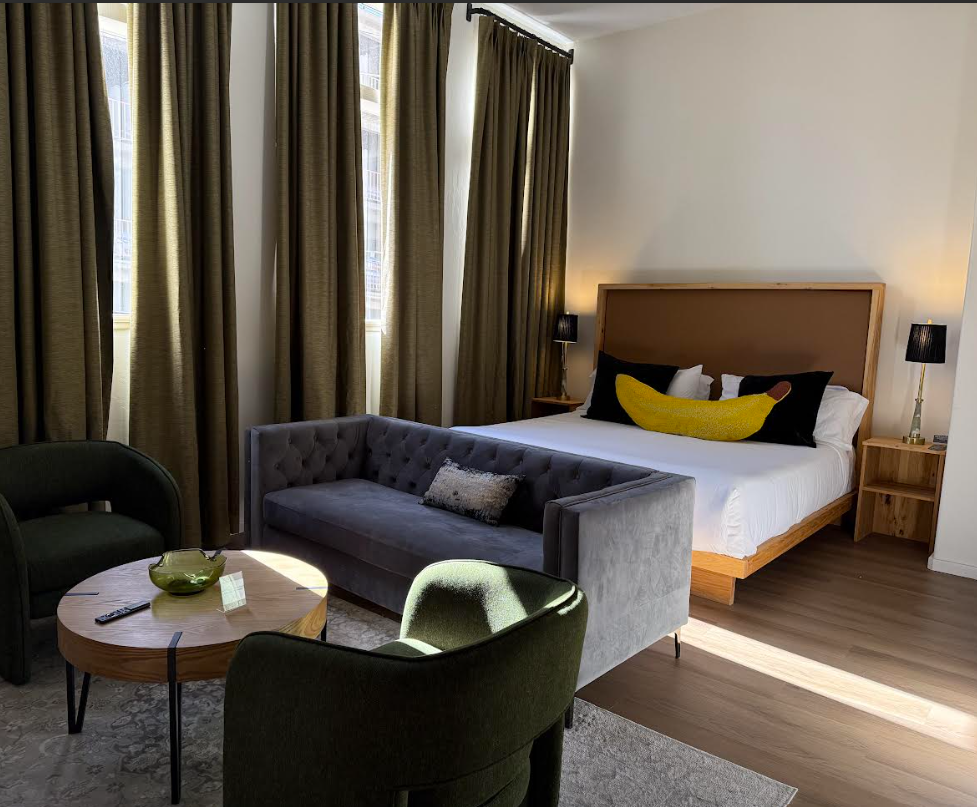 A gray tufted sofa faces a bed with pillows; a coffee table with a green bowl is in front.