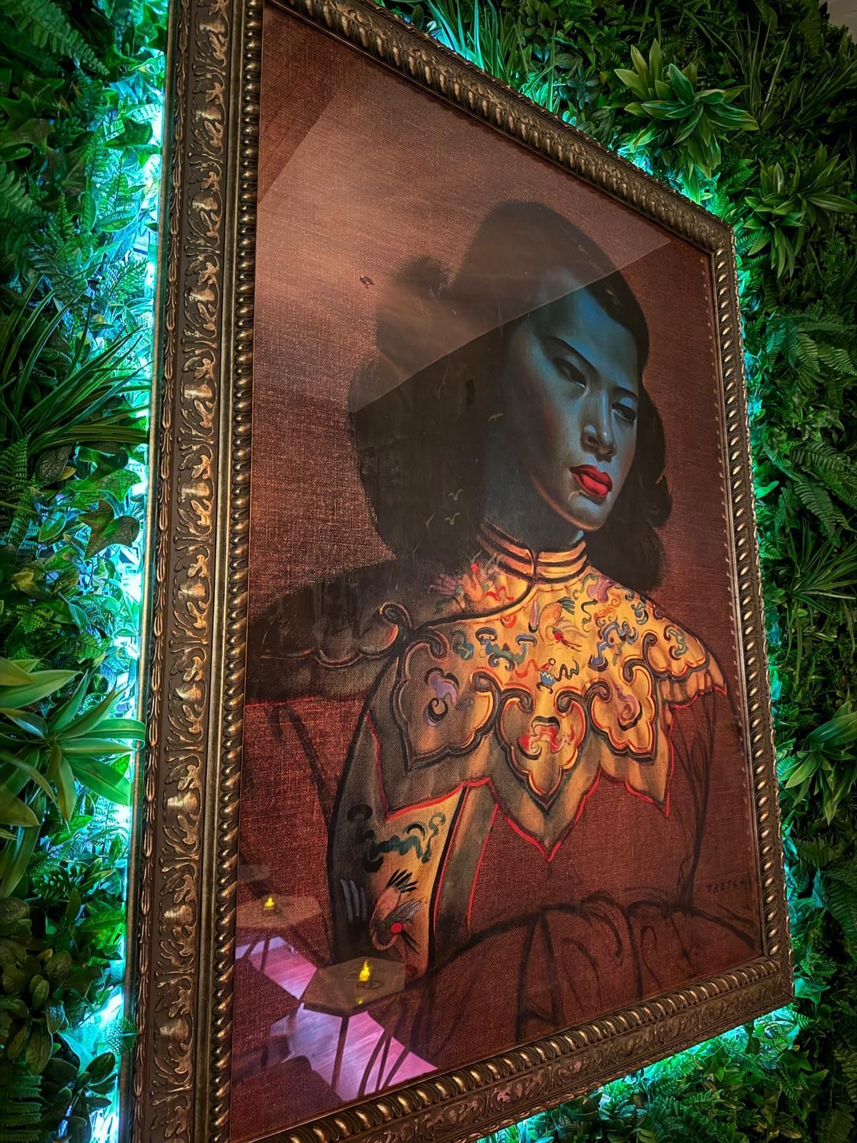 Painting of a woman with red lips and a decorative collar in a gold frame, set against a green wall.