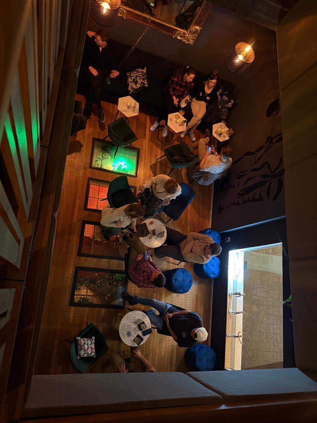 Overhead view of a crowded bar with people gathered around small tables, moody lighting.