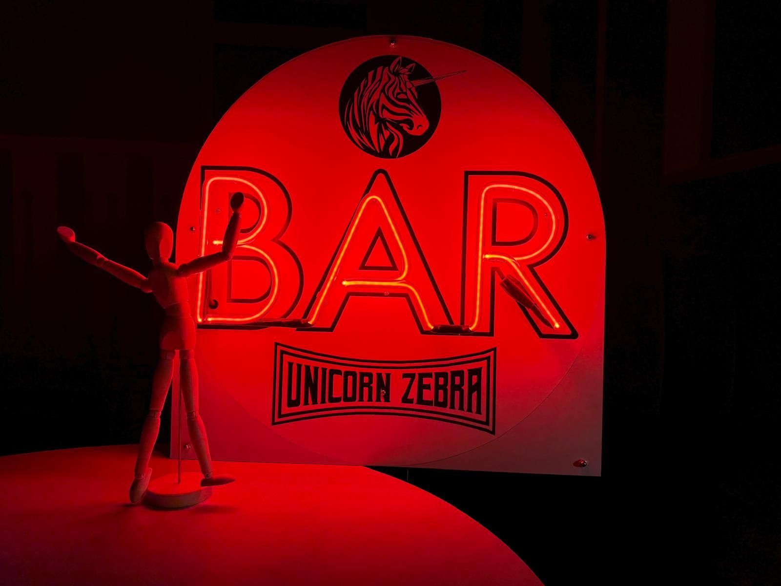 Wooden figure with arms raised in front of a neon red 