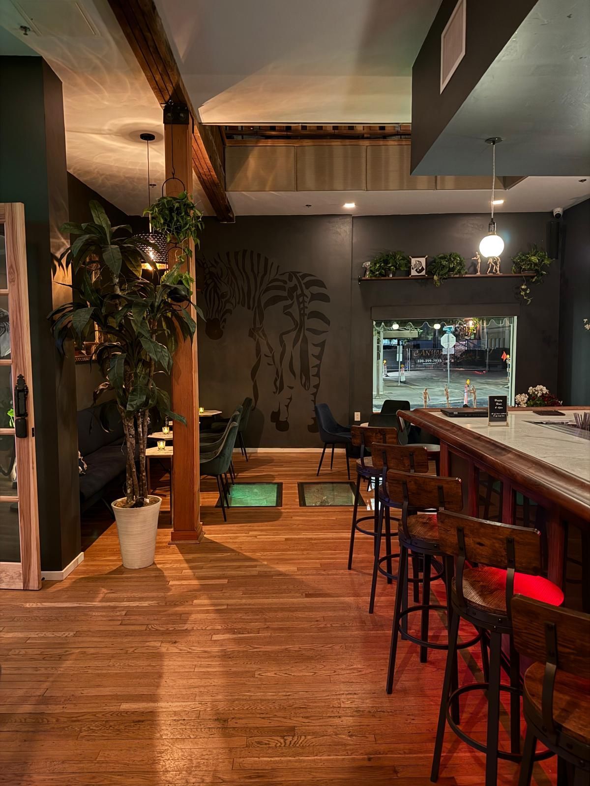 Restaurant interior with bar stools, wooden floor, and a dark wall with a tree design.