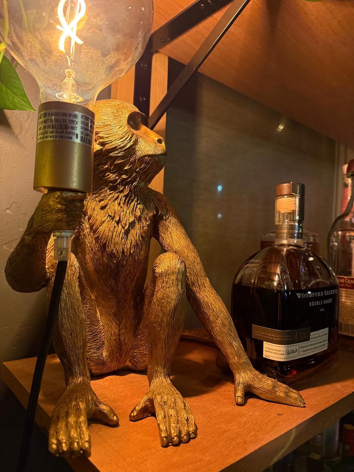 Golden monkey lamp next to a whiskey bottle on a wooden shelf.
