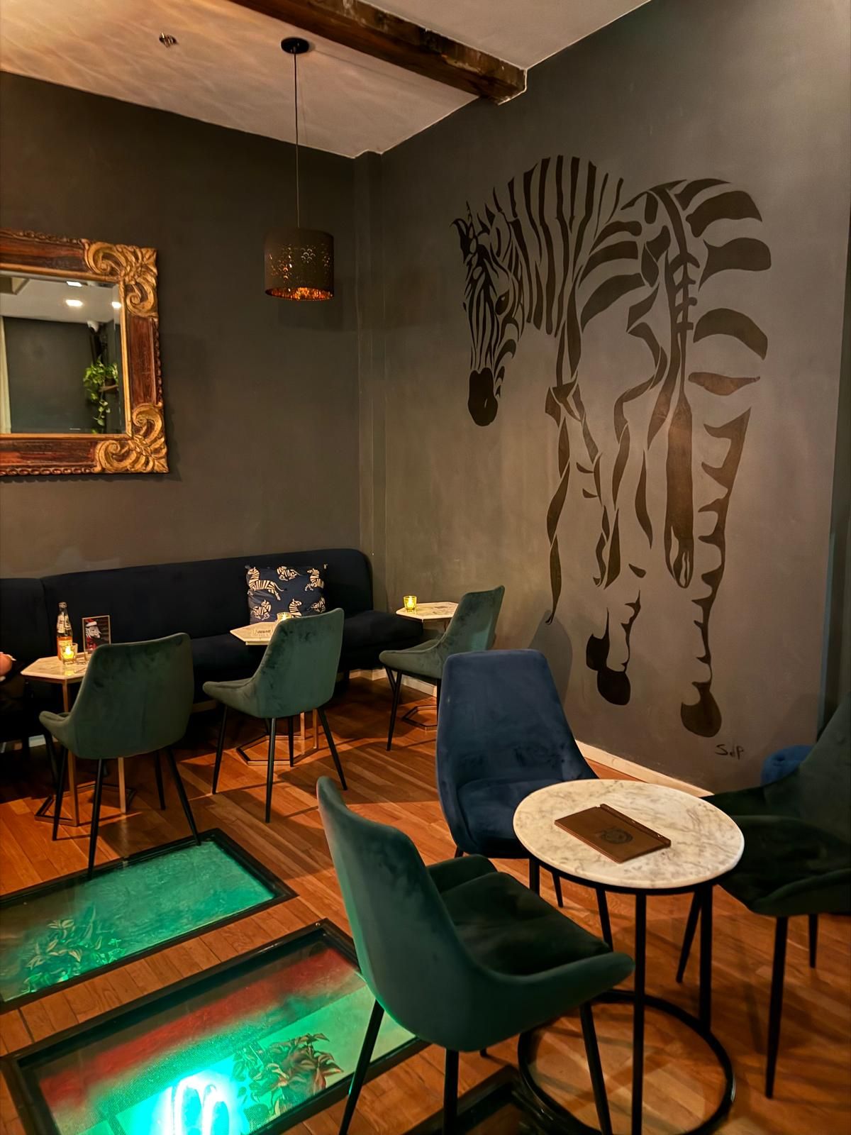 Interior of a bar with blue velvet chairs and zebra mural on dark gray wall.
