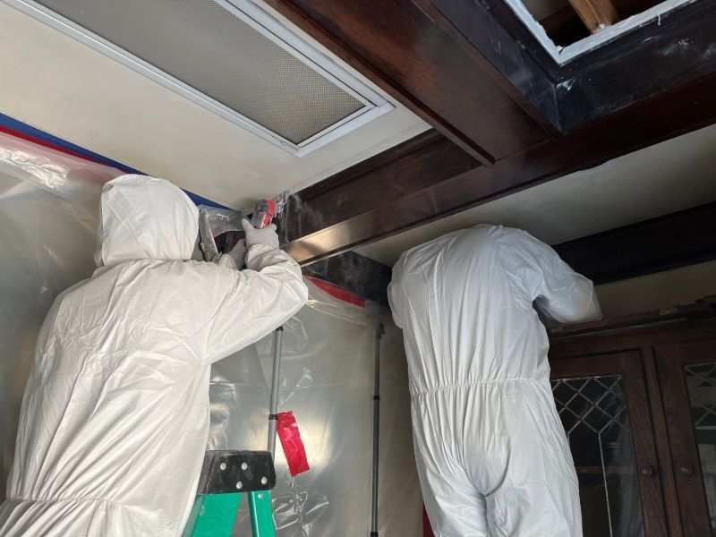Two men in white suits are working on a ceiling in a room.