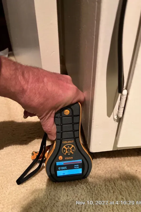 A person is holding a measuring device in front of a refrigerator.