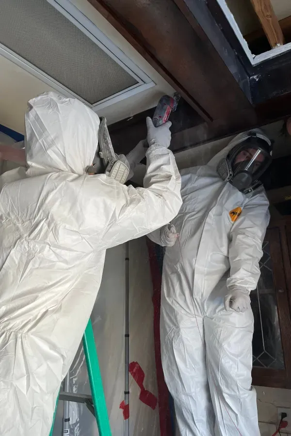 Two people in protective suits are working on a ceiling.