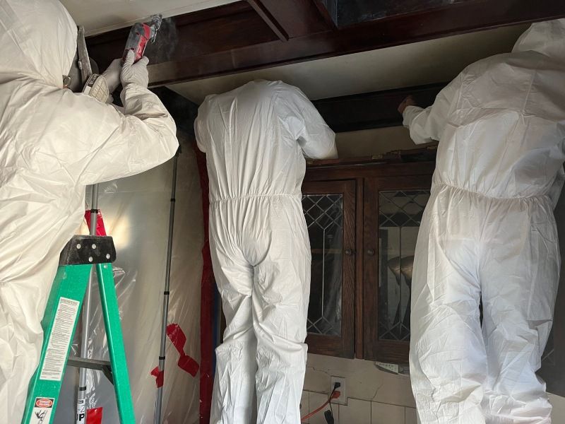 A group of people in protective suits are working on a kitchen ceiling.