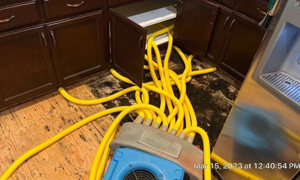 A kitchen with a lot of yellow hose coming out of the cabinets.
