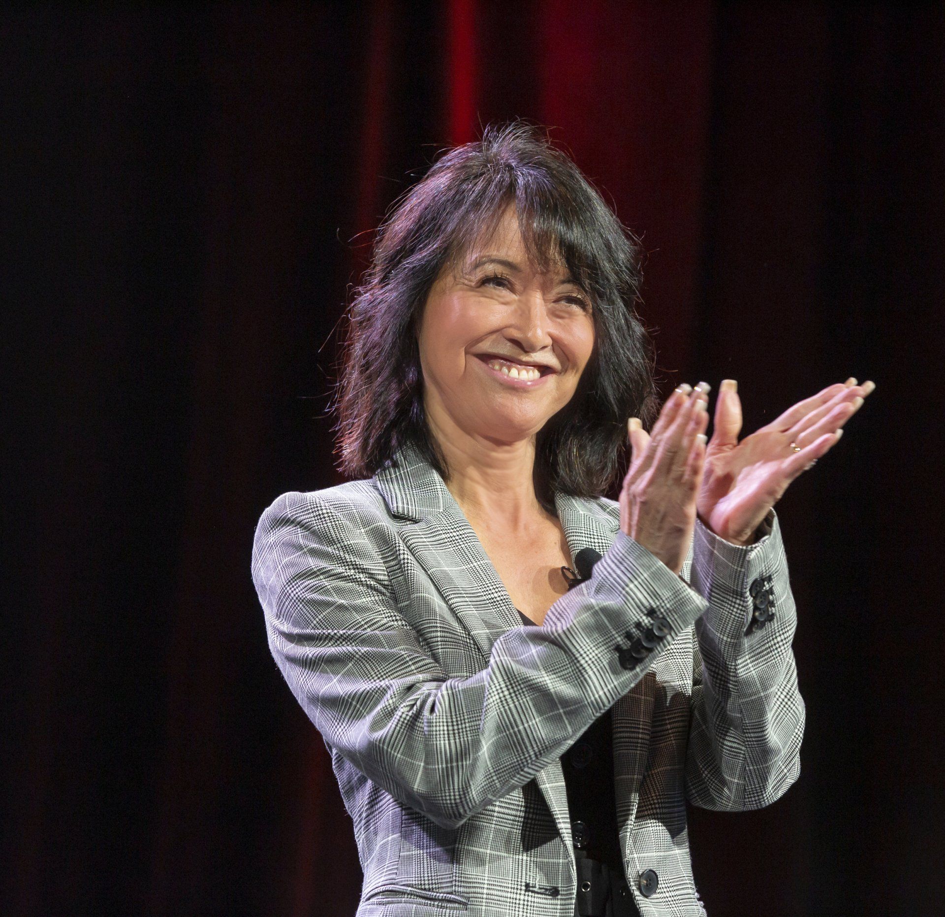 A woman in a grey jacket is smiling and clapping her hands