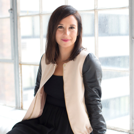 A woman wearing a black dress and a white vest is sitting in front of a window