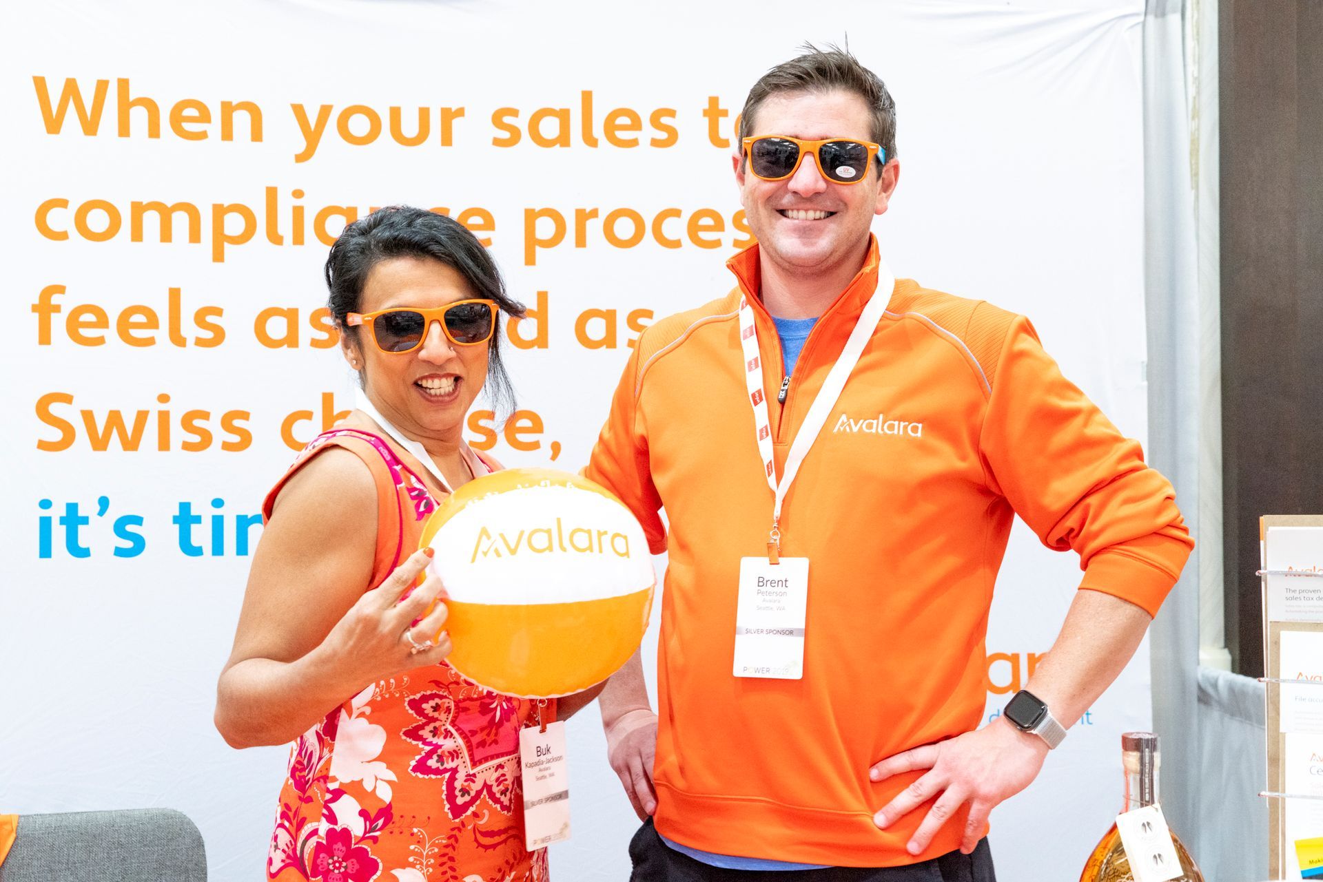 Avalara Booth featuring a woman and a man both wearing orange attire and holding a orange and white ball with 'Avalara' written on it.