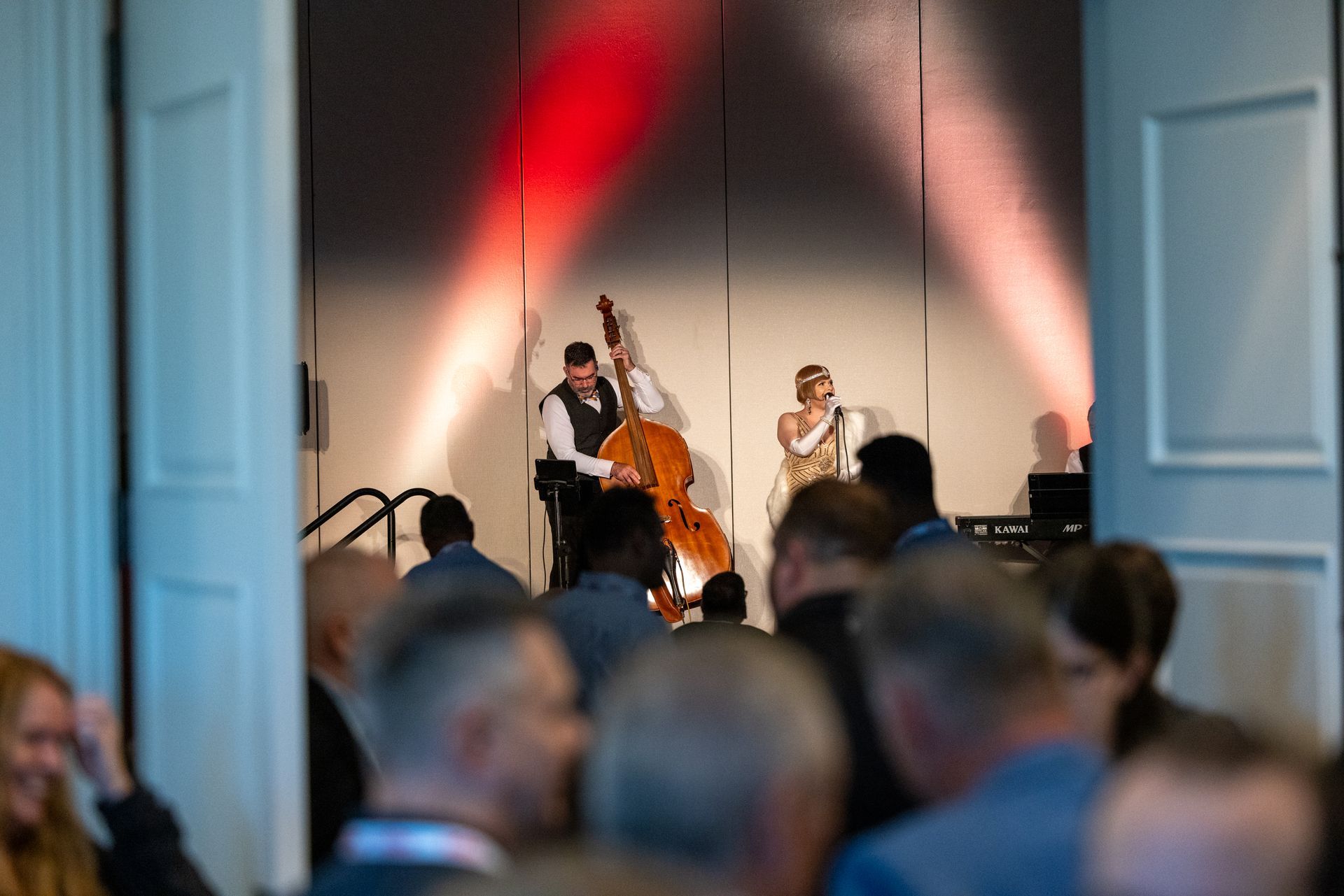 open doors on either side of the photo open to a jazz trio on the stage. Lights form a peak behind them