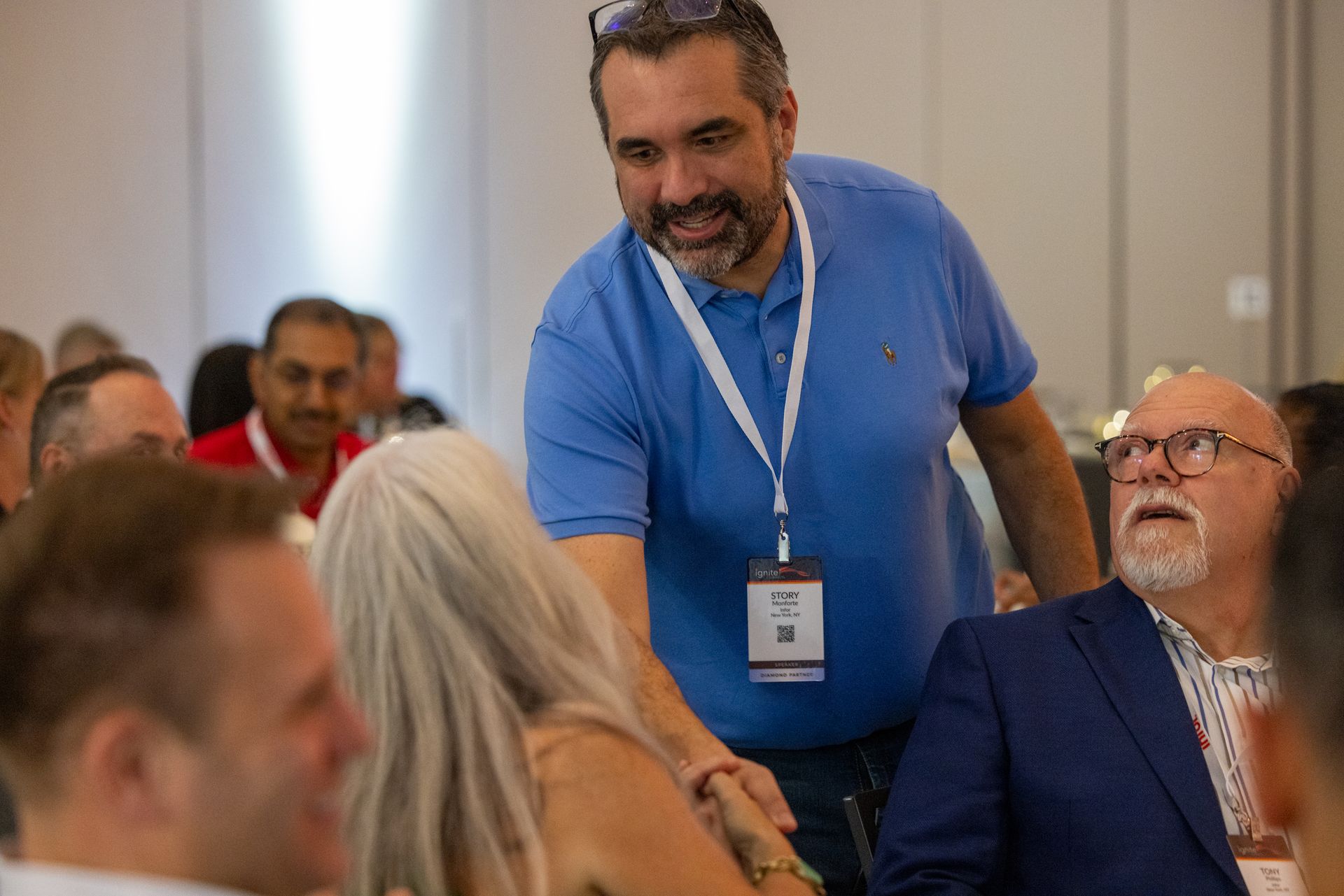 A man in a blue shirt wearing a badge on a lanyard, leans forward, smiling at a woman 