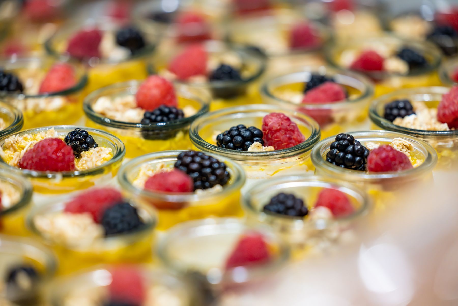 Small glass dishes filled with yellow dessert, topped with crumble, raspberries, and blackberries.