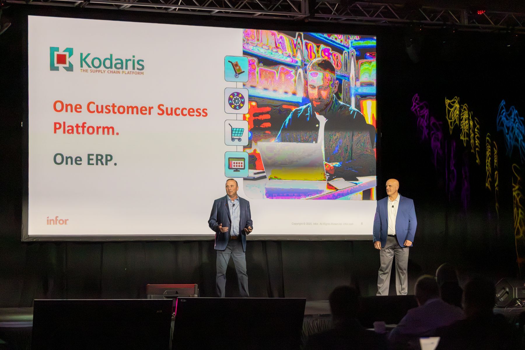 Two men presenting on a stage with a screen displaying "Kodaris" logo and text: "One Customer Success Platform. One ERP."