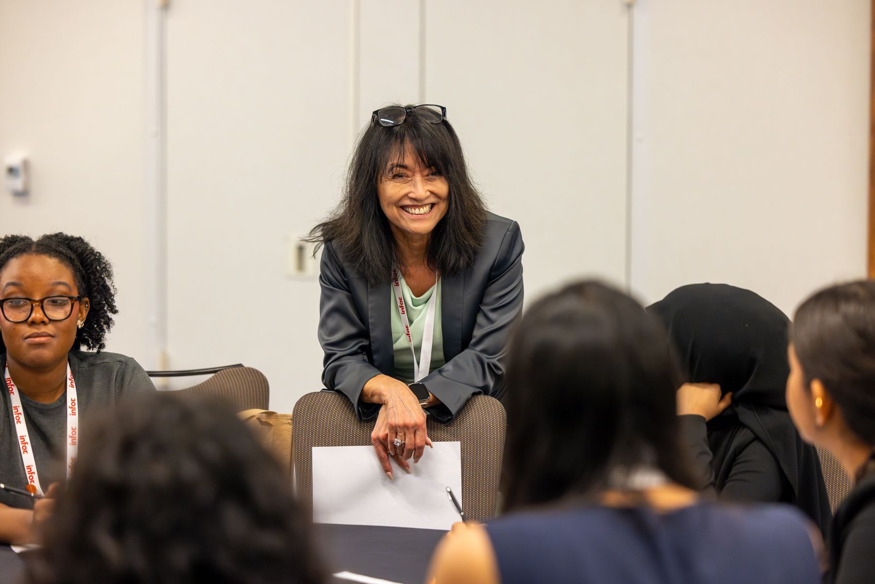 Woman smiling, seated, talking to group of people at a conference table.