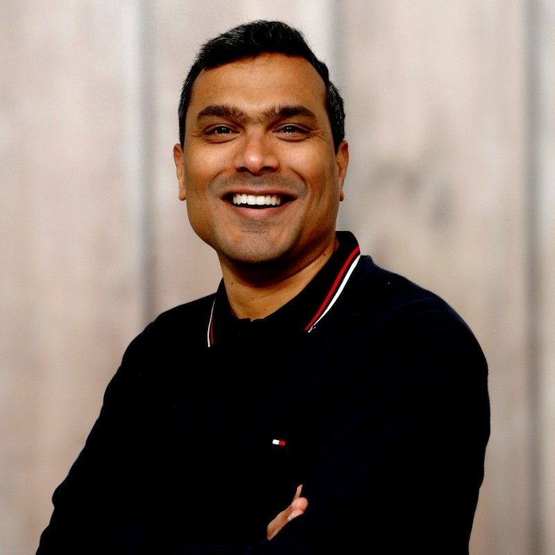 A man in a black shirt is smiling with his arms crossed