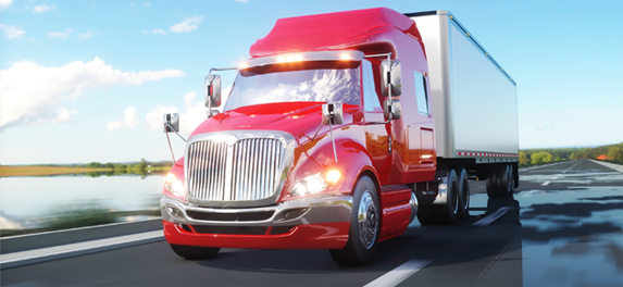 Red semi-truck driving on a highway, bright daylight, blue sky, water and trees in the distance.