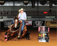 Woman on a horse racing around a barrel in an arena. The horse and rider are turning sharply.