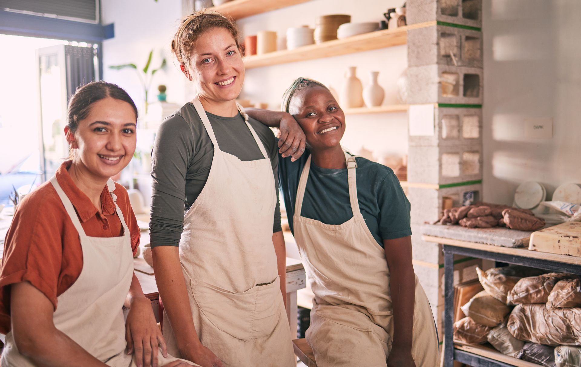 Three women are posing for a picture in a pottery studio.