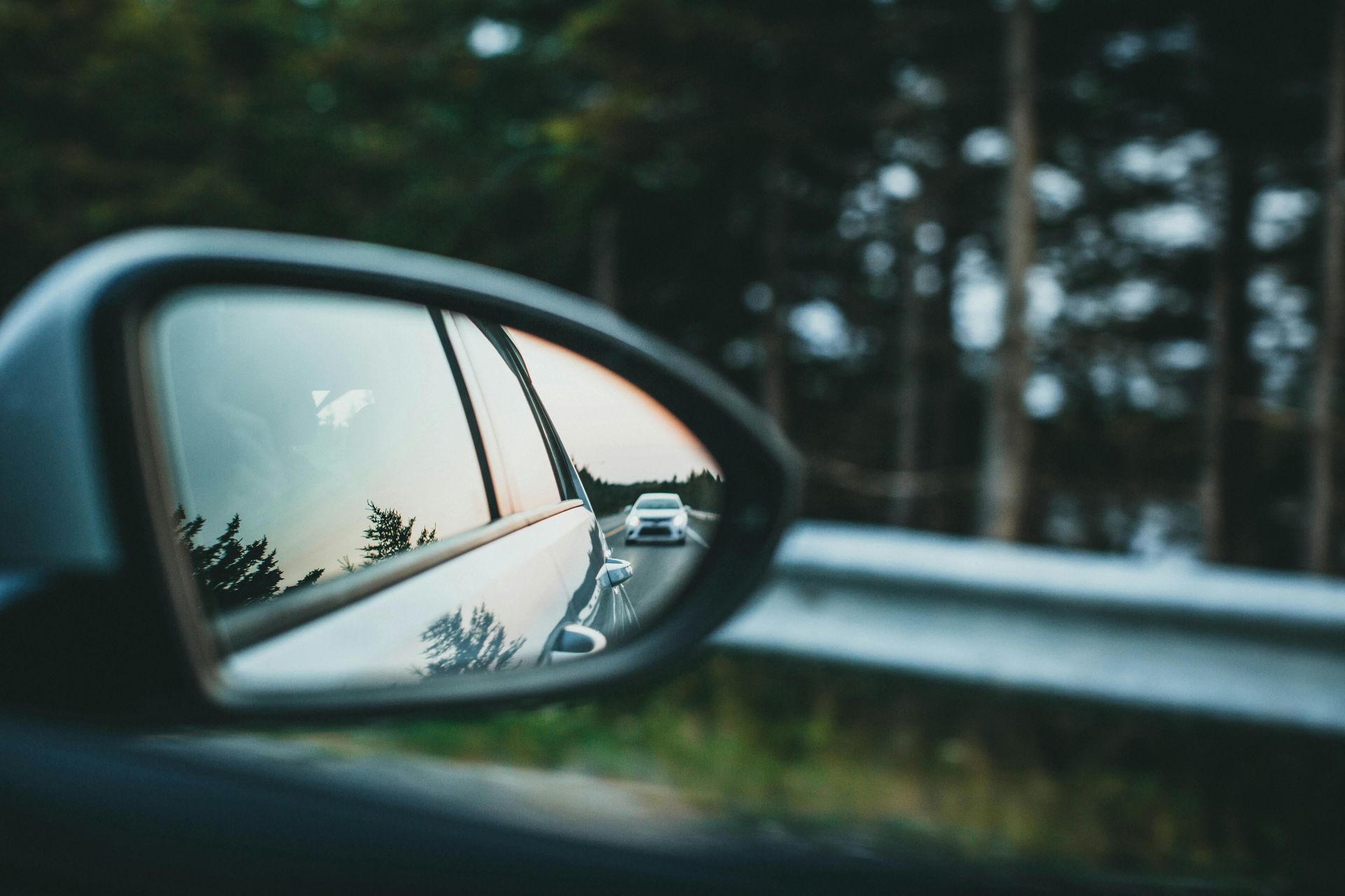 A car is driving down a road in the rear view mirror.