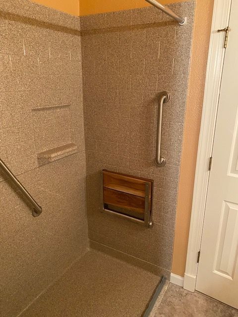A walk in shower with a wooden seat and stainless steel handles.