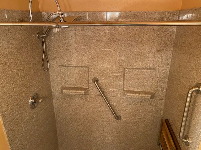 A bathroom with a walk in shower with a stainless steel handle.