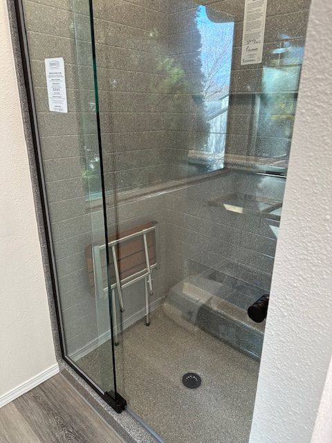 A bathroom with a walk in shower with a chair in it.