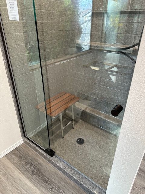 A shower with a wooden bench in it and a glass door.