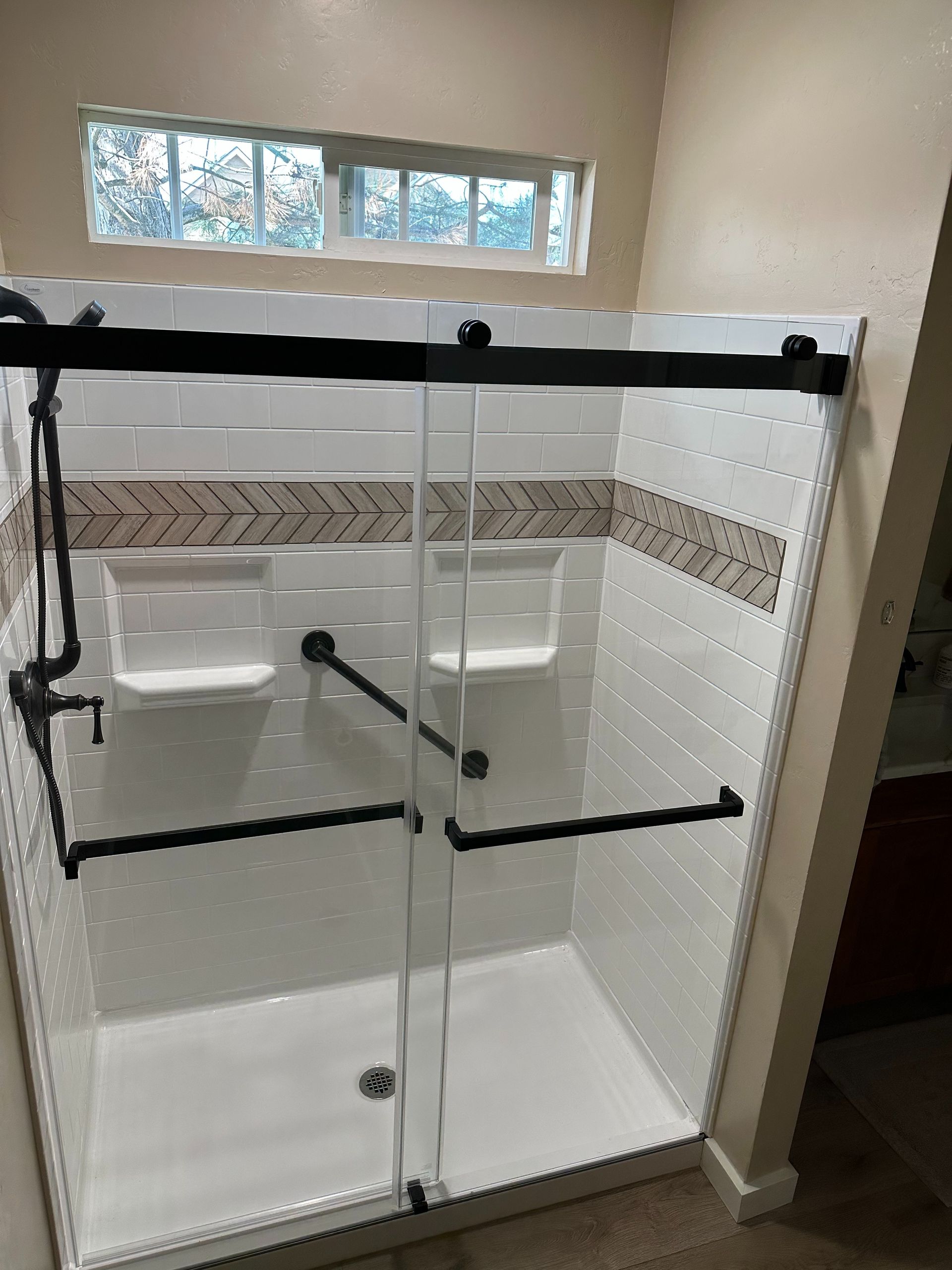 A bathroom with a walk in shower with sliding glass doors and a window.
