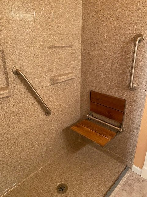 A shower with a wooden seat and stainless steel handles.