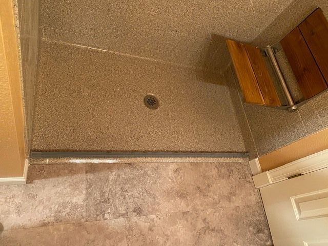 A bathroom with a walk in shower with a wooden seat.