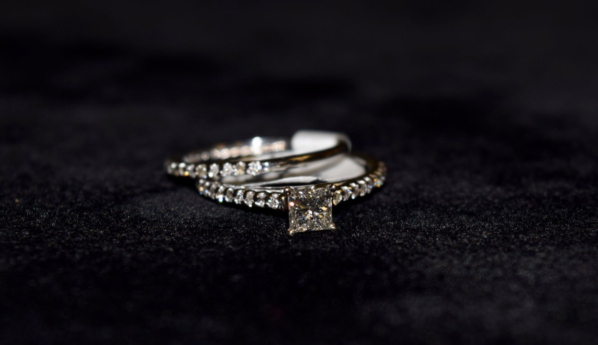 A close up of a wedding ring and engagement ring on a black surface.