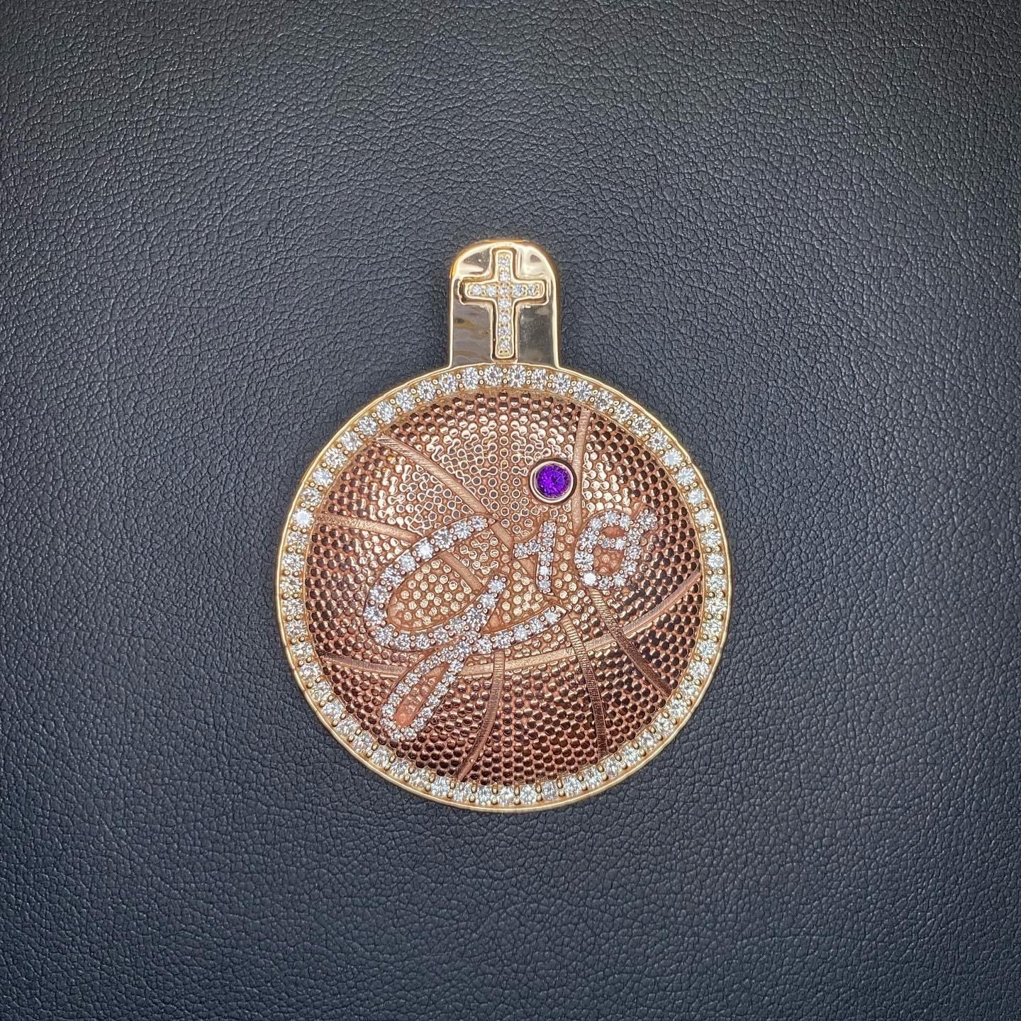 A gold pendant with a cross on it is on a black surface.