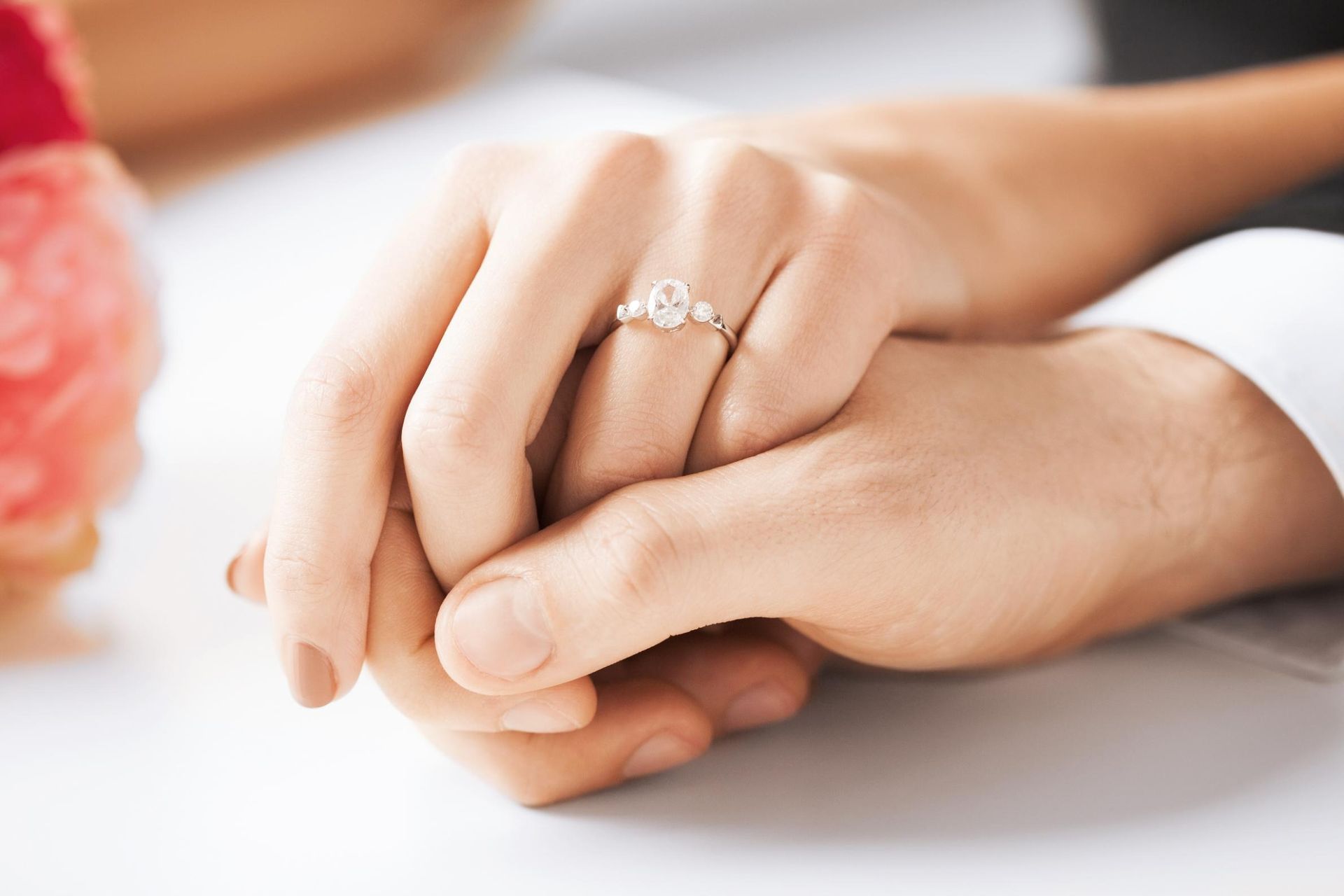 A man and a woman are holding hands and the woman has an engagement ring on her finger.