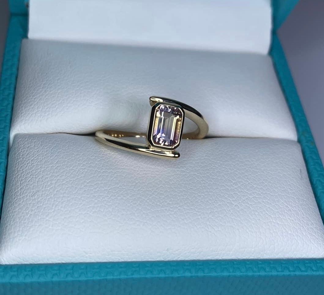 A gold ring with an emerald cut diamond is in a box.