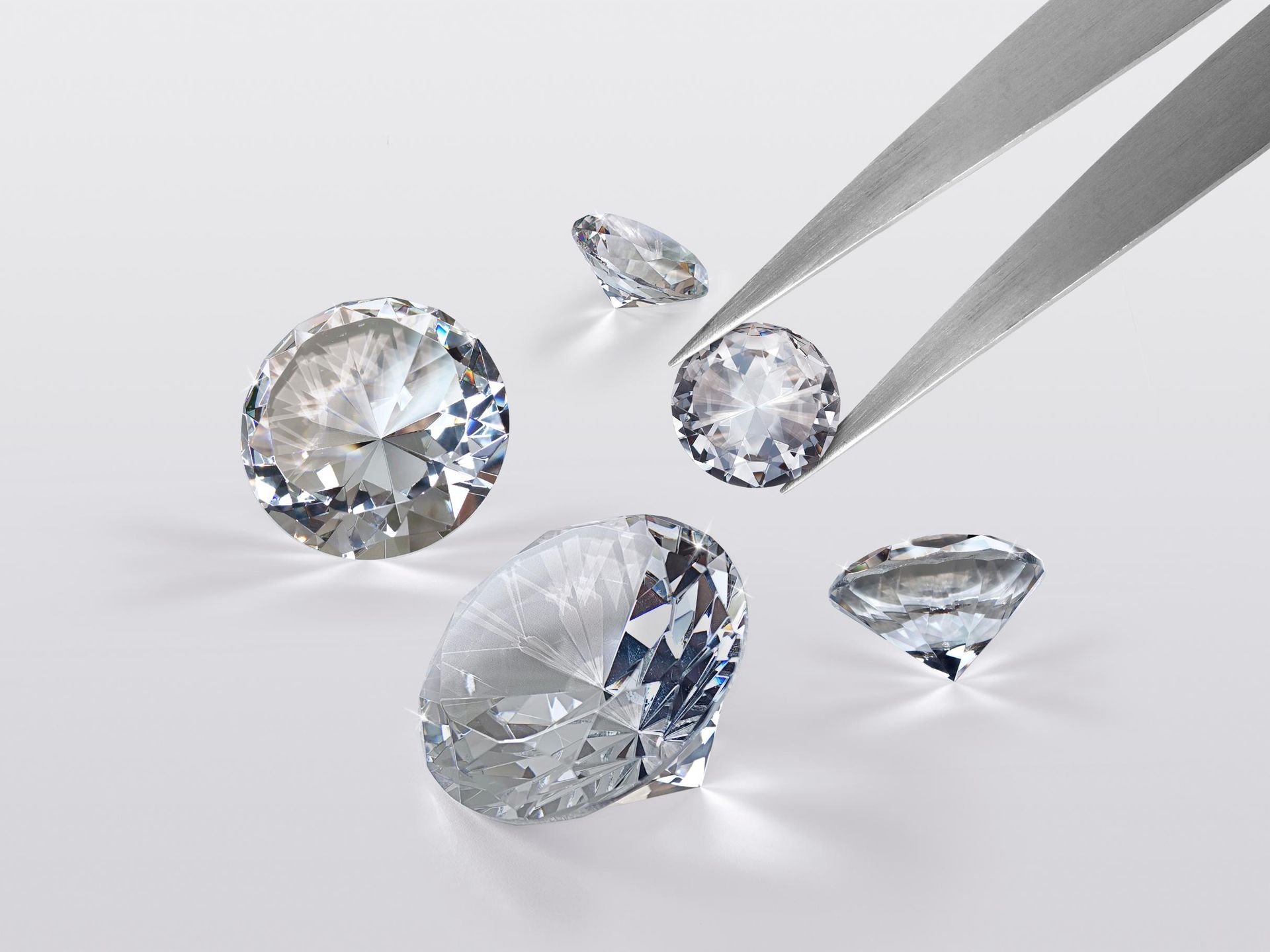A pair of tweezers holding three diamonds on a white surface.