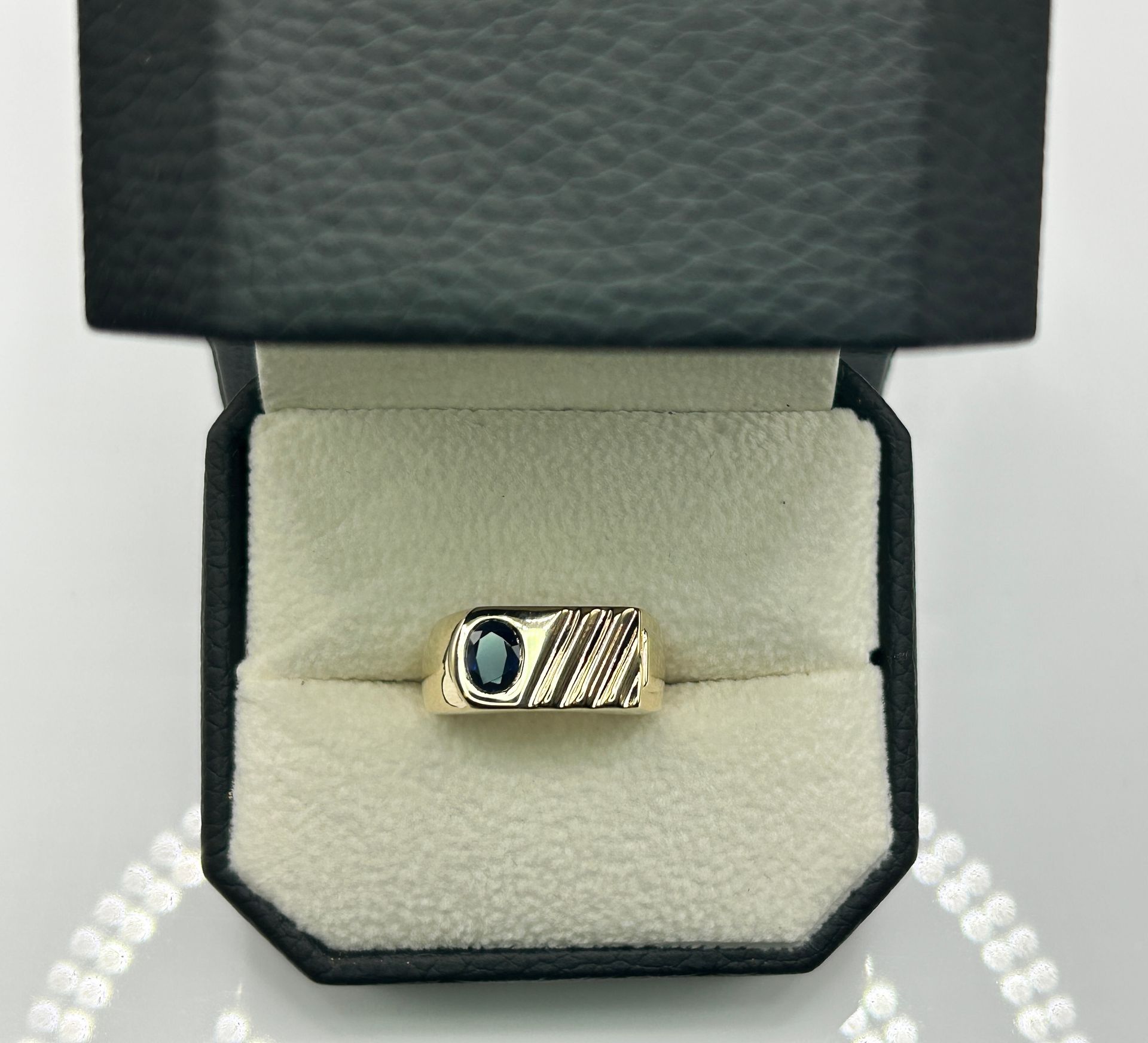 A gold ring with a blue stone is in a black box.