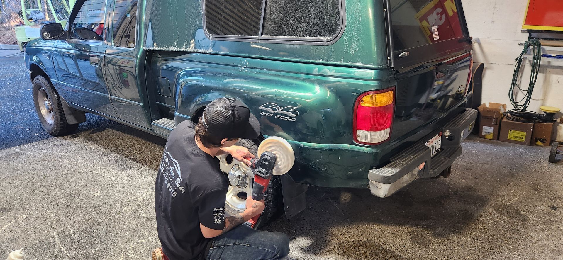 Person polishing the rear bumper of a green SUV in a garage, with tools nearby. | Tripp's Auto Body