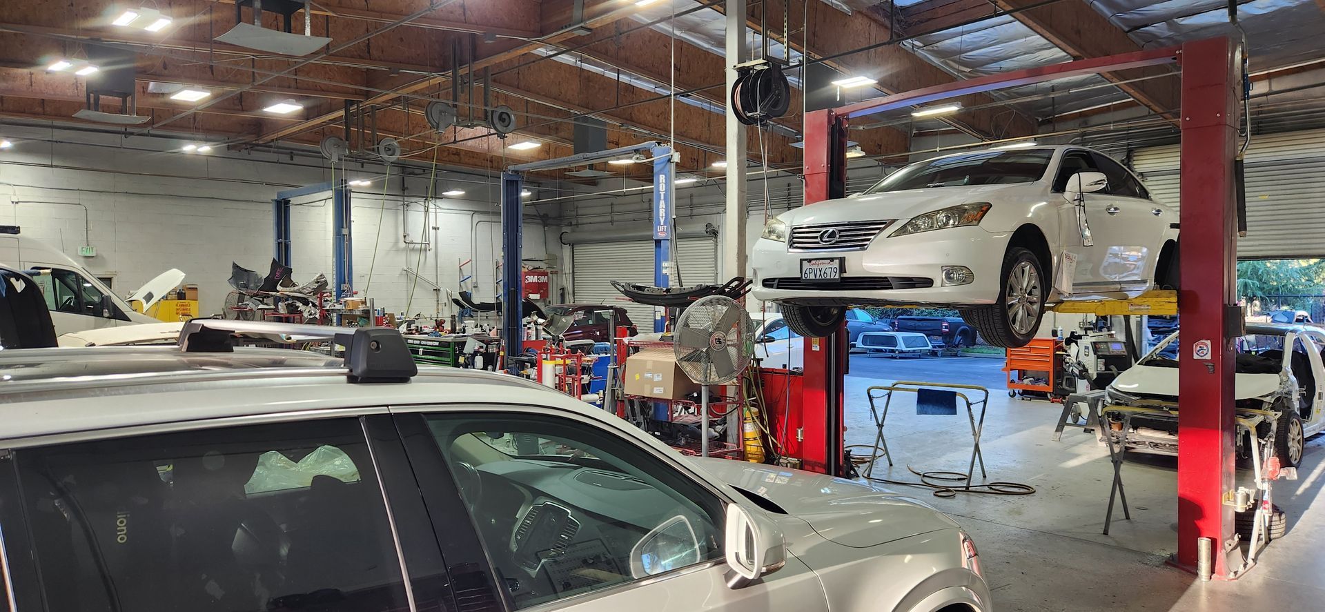 Auto repair shop with cars on lifts and a silver car in the foreground, tools and equipment around the garage | Tripp's Auto Body