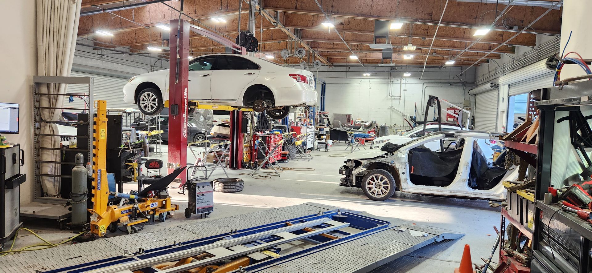 Auto repair shop with lifts, a white car on a hoist, and a car with its doors open on the floor | Tripp's Auto Body