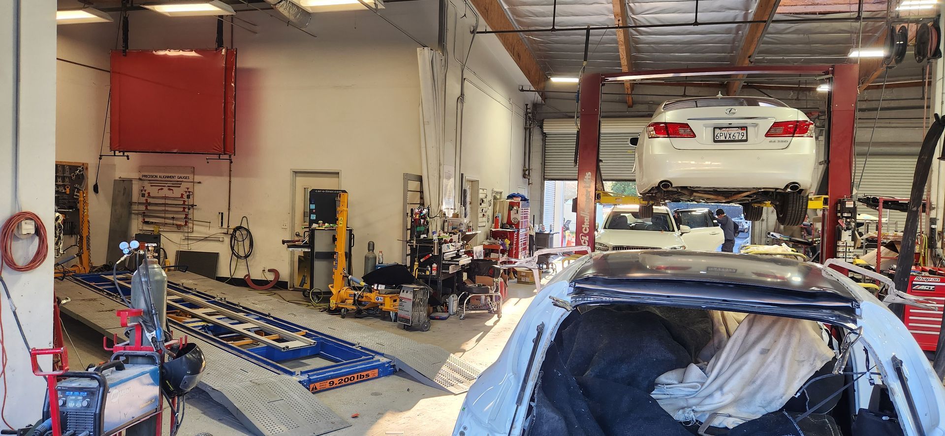 Auto repair shop interior with car lifts, tools, and a white car raised above another vehicle | Tripp's Auto Body