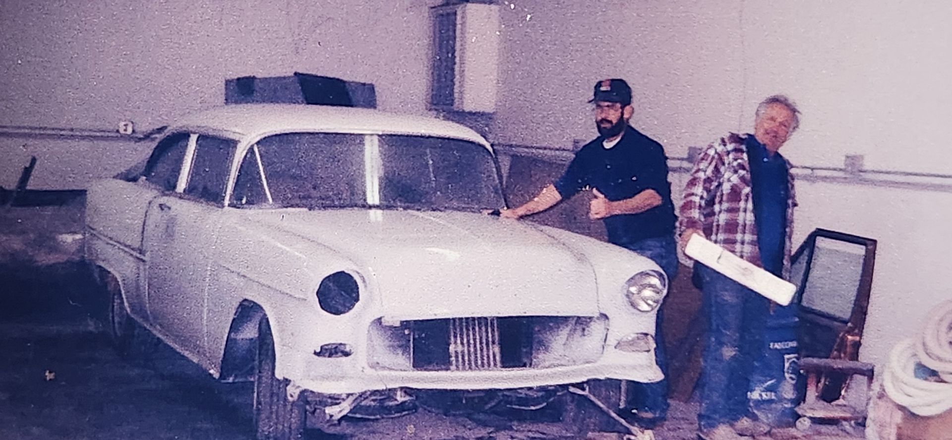 Two men beside a white car with the front damaged in a garage. | Tripp's Auto Body