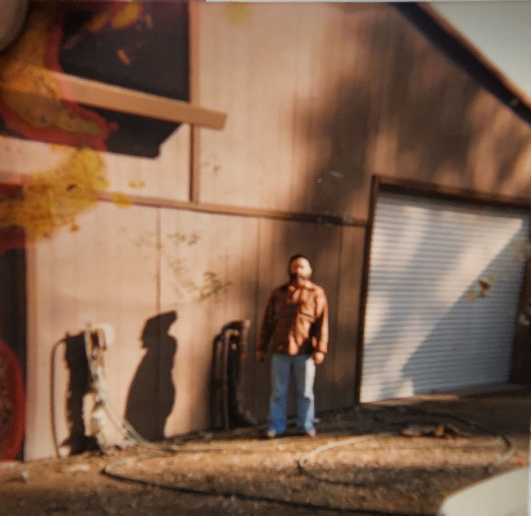 Man standing against a tan building beside a closed metal garage door in sunlight | Tripp's Auto Body