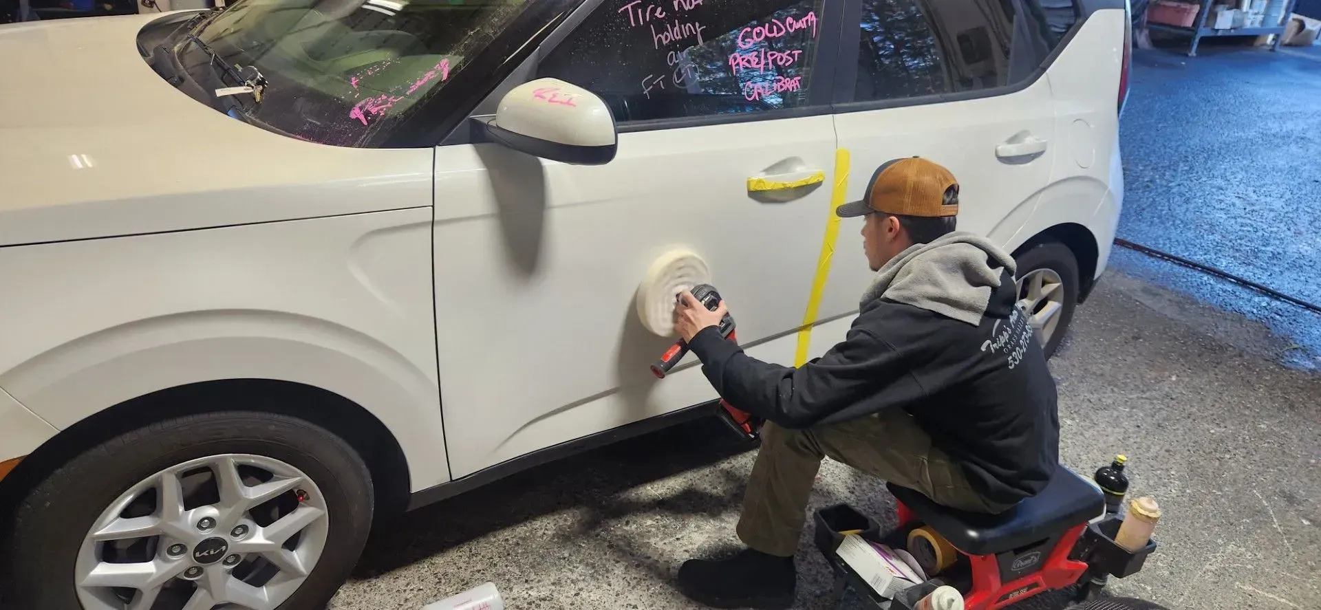 Person in a yellow helmet washing a white SUV at a car wash. | Tripp's Auto Body