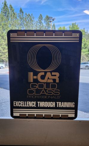 Wall sign for Car Golf Class Professionals with the slogan “Excellence Through Training” on a beige wall. | Tripp's Auto Body
