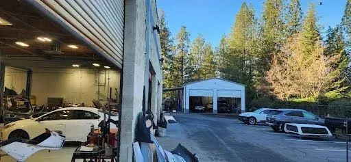 Open garage and workshop beside a driveway with parked cars and trees in the background | Tripp's Auto Body