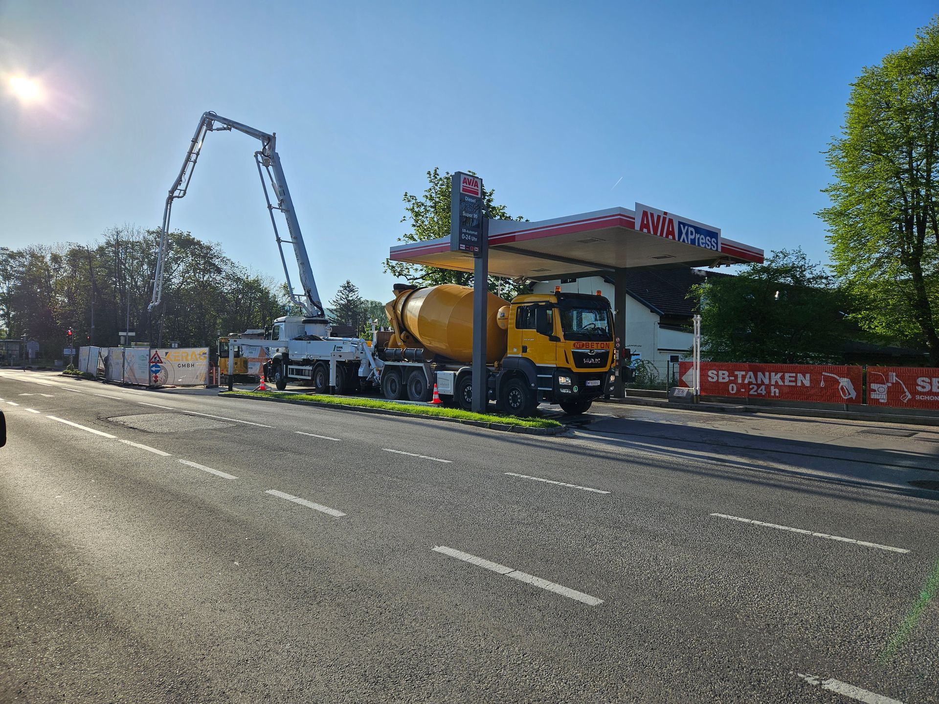 Betonmischer mit Ausleger gießt Zement in der Nähe einer Tankstelle unter blauem Himmel.