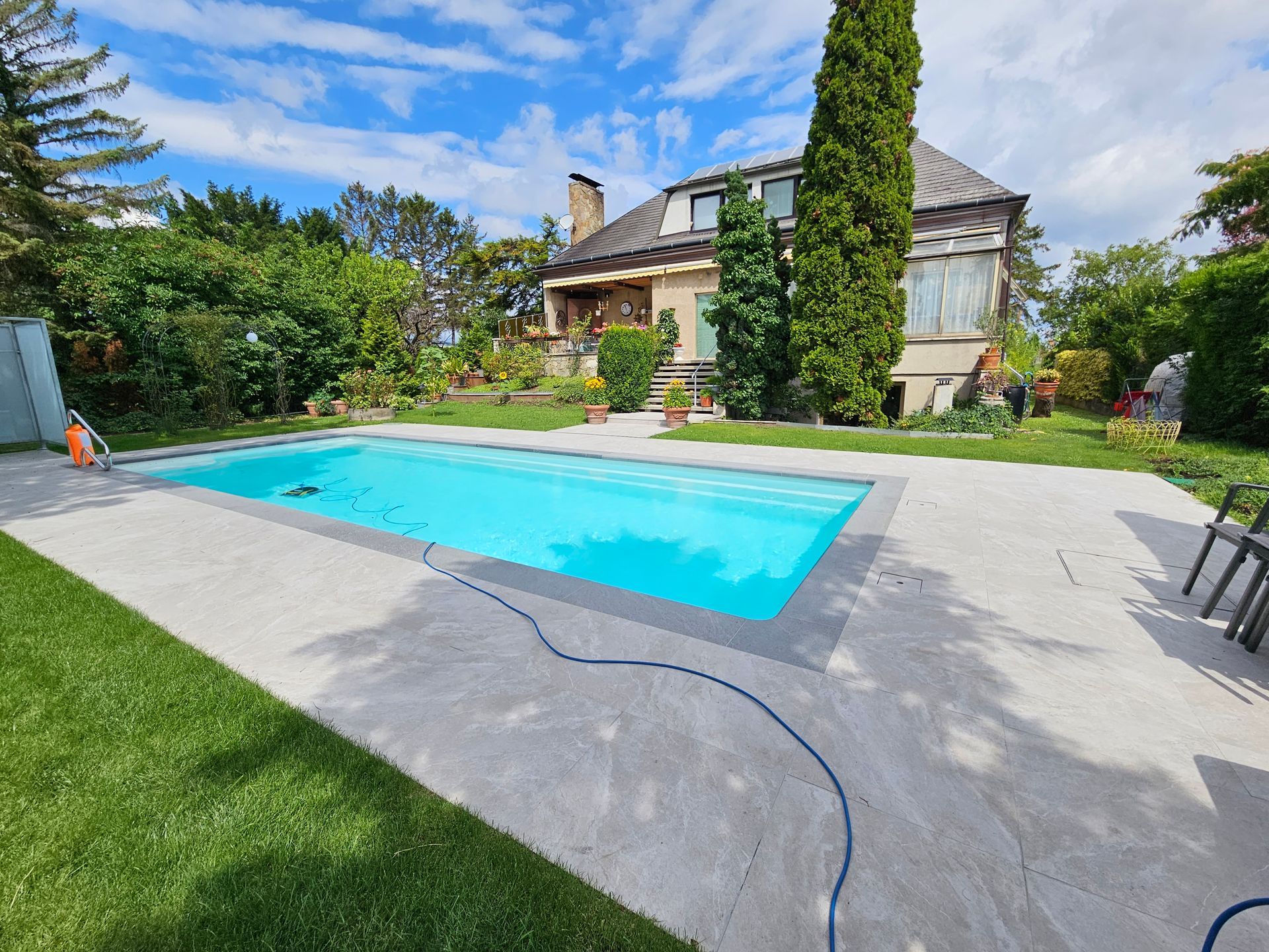 Hinterhof mit Pool, Haus, grünem Rasen und blauem Himmel.