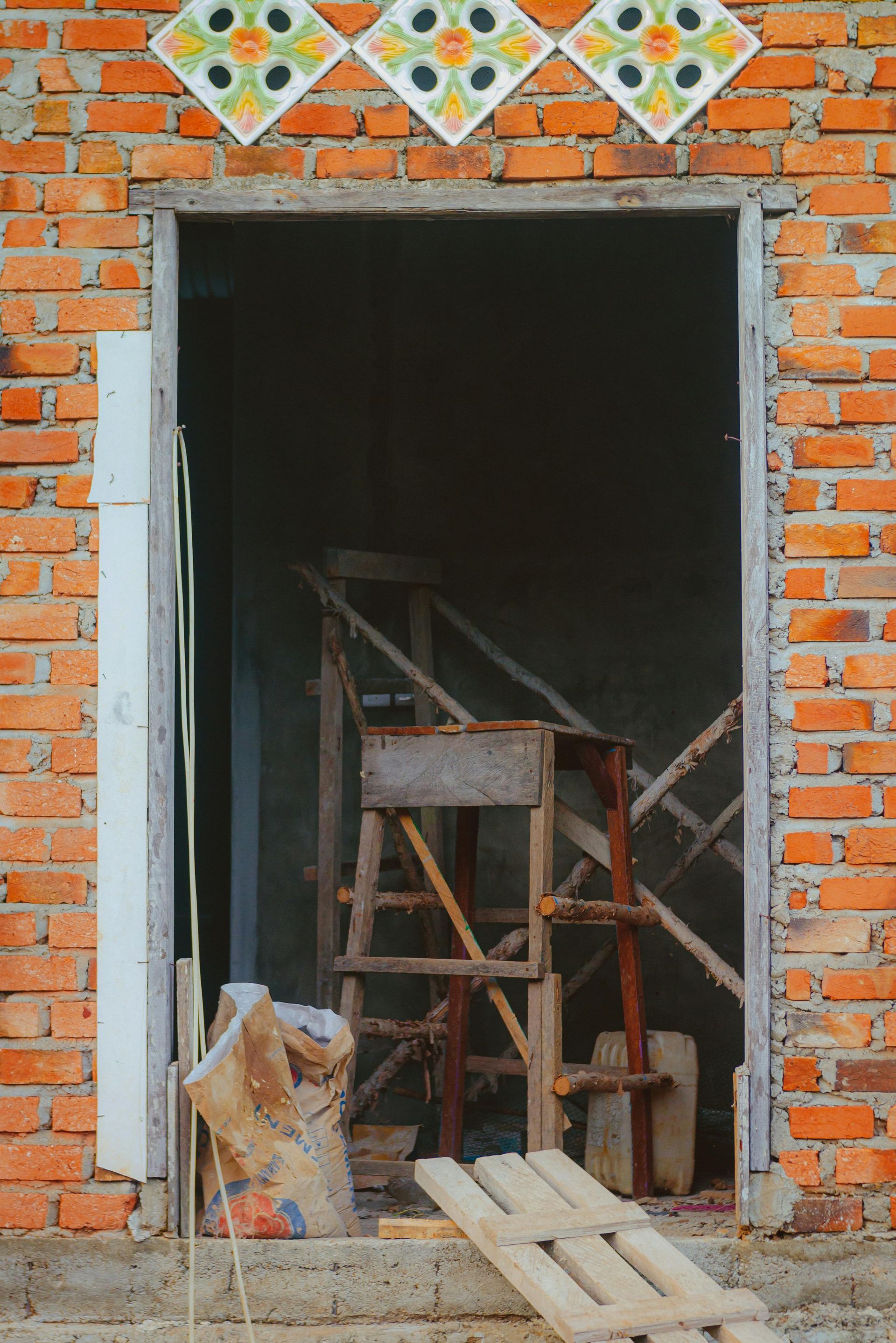 A wooden ladder is sitting in the doorway of a brick building under construction.